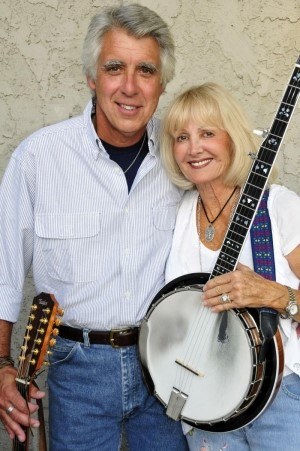 Man holding a guitar and woman holding a banjo stand next to each other smiling